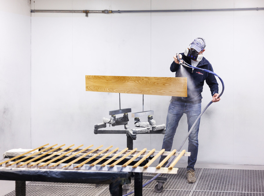 Mann in einer Lackiererei spritzt ein Holzstück