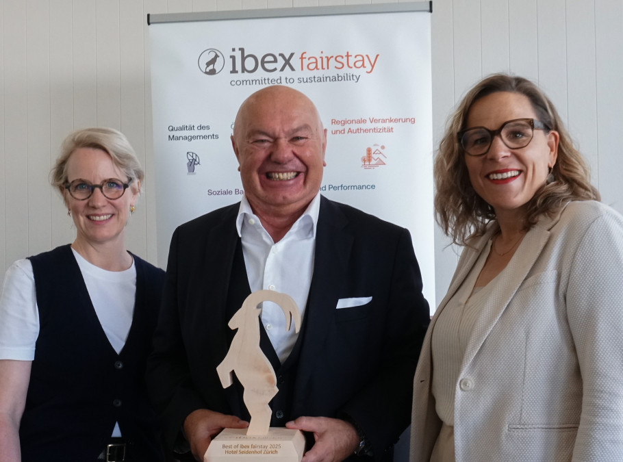 Drei Personen lächeln in die Kamera, der Mann in der Mitte hält die Auszeichnung von ibex fairstay
