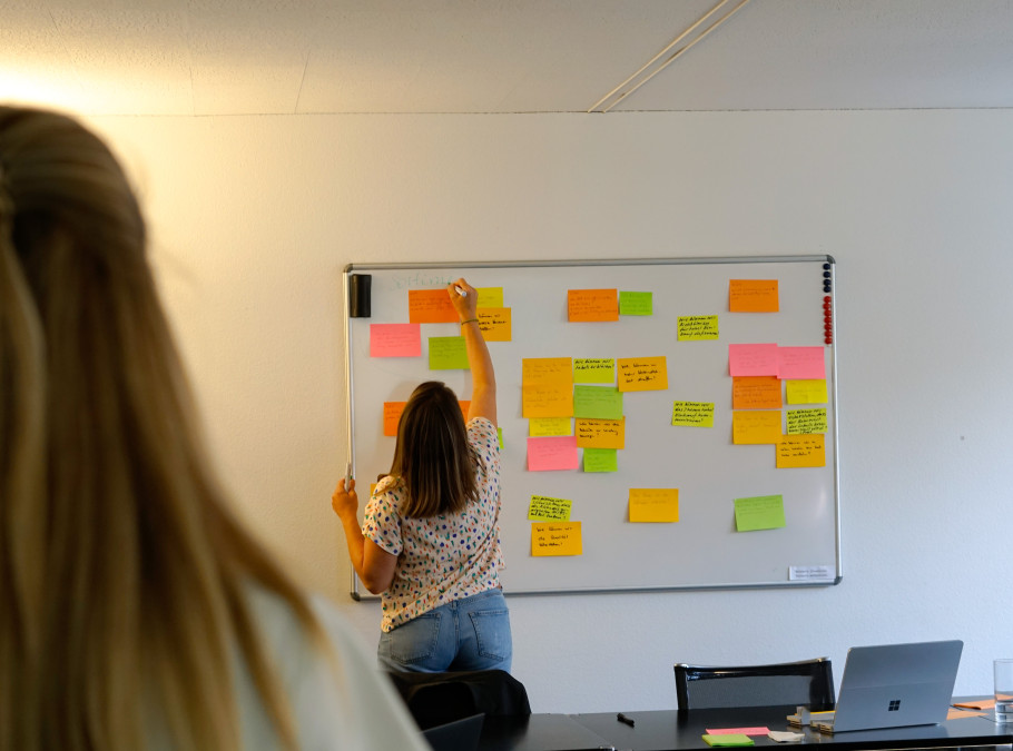 Frau an einem Whiteboard klebt Zettel hin