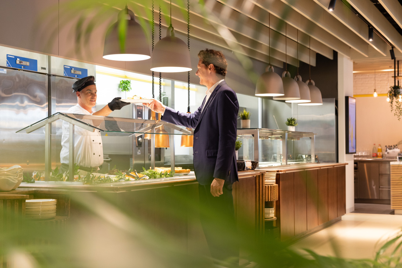 Begegnungsort an einem Buffet, Koch gibt frisches Essen an eine Person im Businessanzug