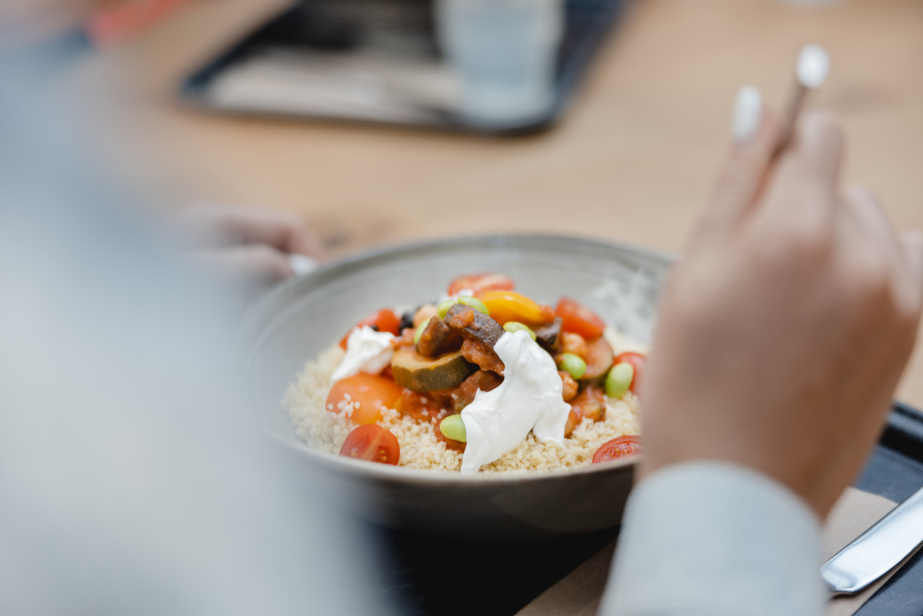 Person isst eine ausgewogene Bowl mit Gemüse und Couscous