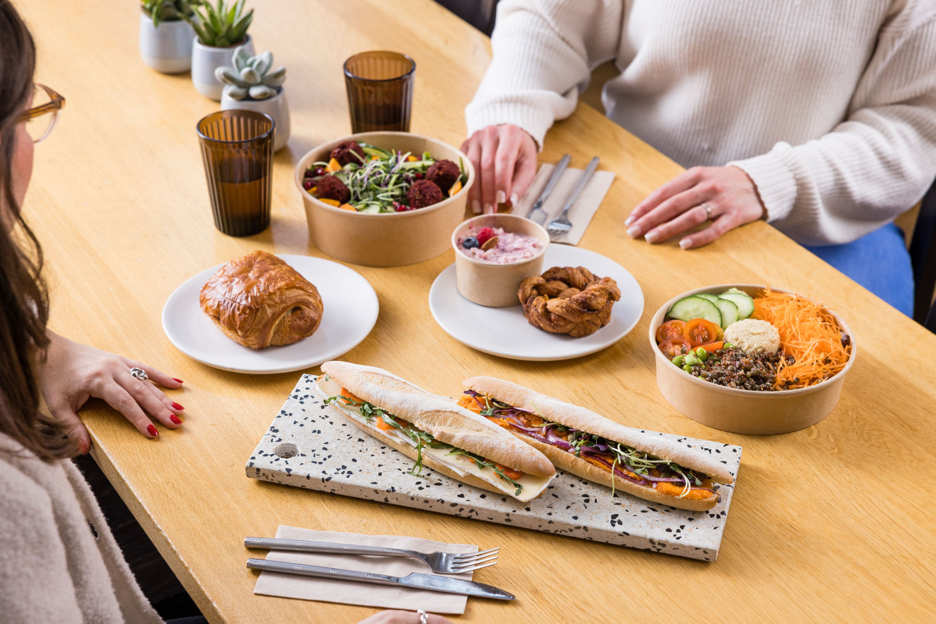Tisch mit zwei Personen und Angebot an Take ou-Speisen in nachhaltiger Verpackung