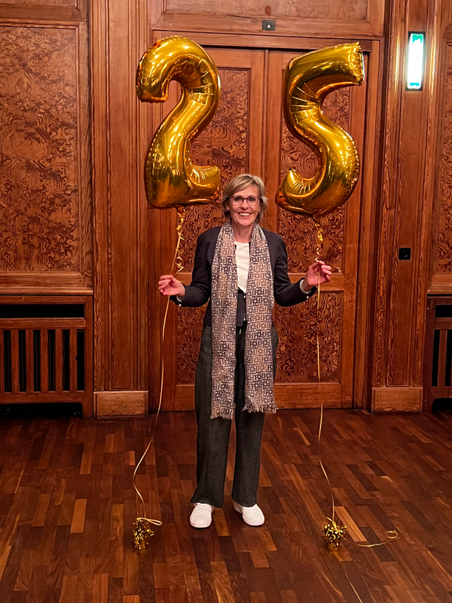 Frau blickt stehend in die Kamera und hält goldene Ballons mit einer 30