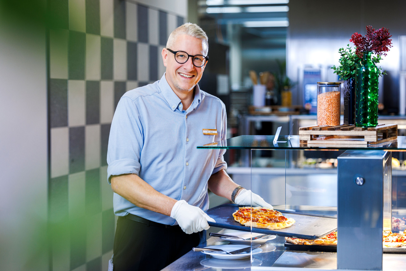 Mann in Serviceuniform füllt ein Speisebuffet mit Pizza auf