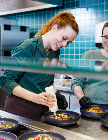 Frau steht in der Küche und fügt Topping auf eine Bowl hinzu