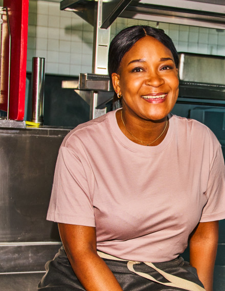 Frau sitzt in einer Gastronomieküche mit Arbeitsbekleidung