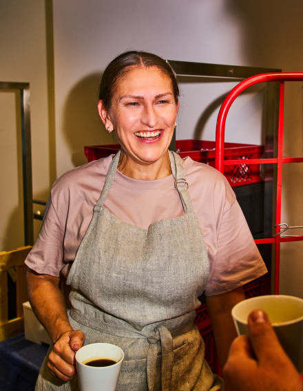 Frau mit Arbeitsbekleidung und Kaffee in der Hand in Gastronomieumgebung