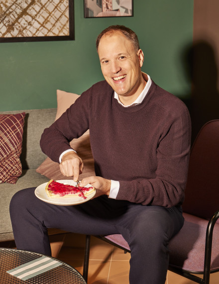 Mann lächelt mit einem Stück Kuchen in die Kamera