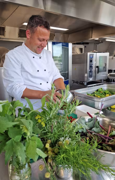 Koch in Küche bei der Zubereitung von Essen mit frischen Kräutern im Hintergrund