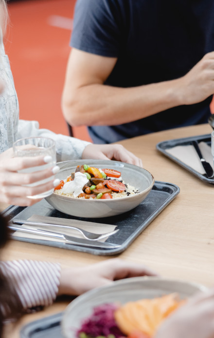 drei Personen an einem Mensatisch mit Mittagsmenüs auf einem Tablar