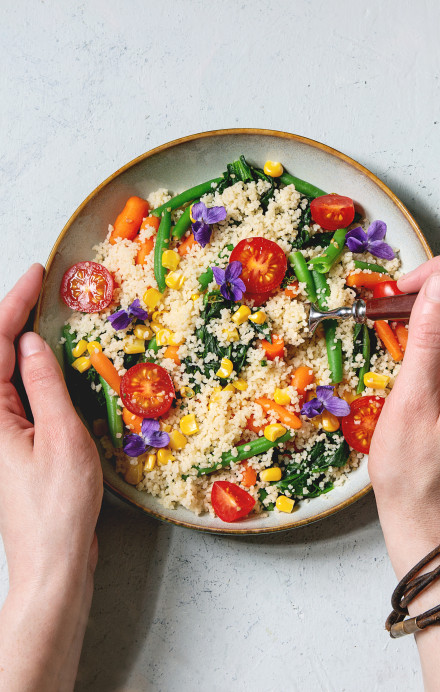 Zwei Hände halten eine Schüssel mit Couscous und diversem Gemüse