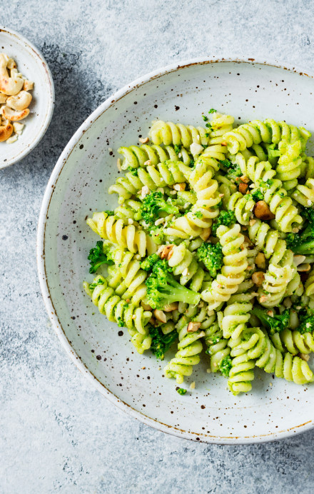 Fusilli mit Broccoli und Cashewnüssen auf einem Teller, daneben eine Schale mit Cashewnüssen