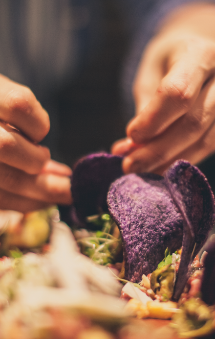 Männliche Hand bereitet ein Gericht mit viel Gemüse zu und setzt Chips aus blauen Kartoffeln darauf