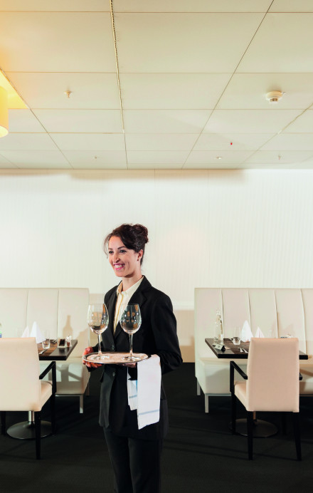 Mitarbeitende in Serviceuniform trägt Tableu mit einem Glas in einem Restaurant