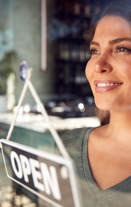 Frau blickt durch eine Fensterscheibe, vor ihr ein Openschild