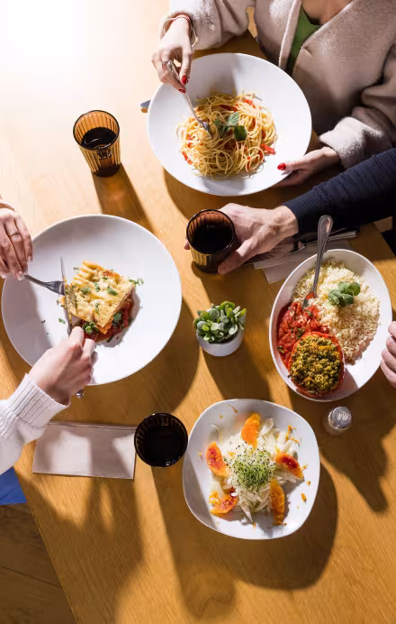 Tisch mit vier Gerichten und Menschen beim Essen