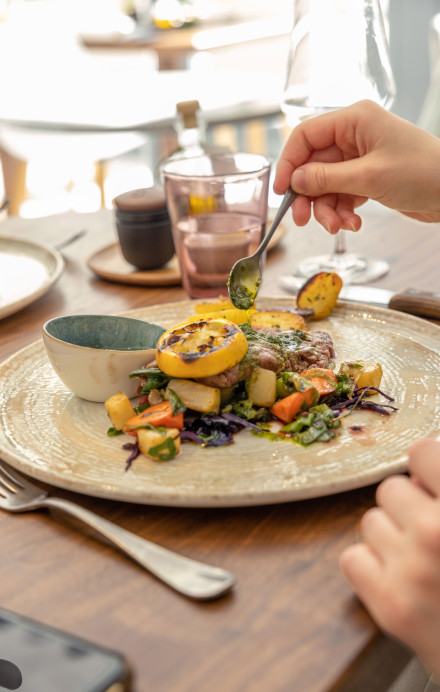 Teller mit weiblichen Händen, die Sauce auf ein Fleischgericht träufeln