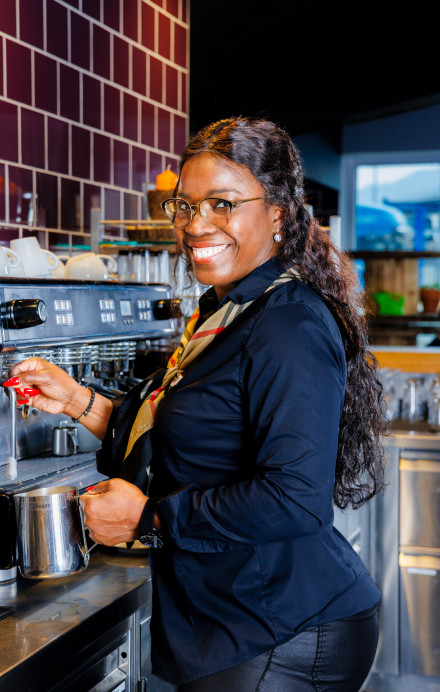 Frau steht an der Kaffeemaschine eines Restaurants und lächelt in die Kamera