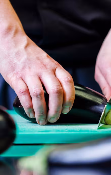 Zwei männliche Hände schneiden eine Aubergine