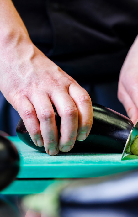 Zwei männliche Hände schneiden eine Aubergine