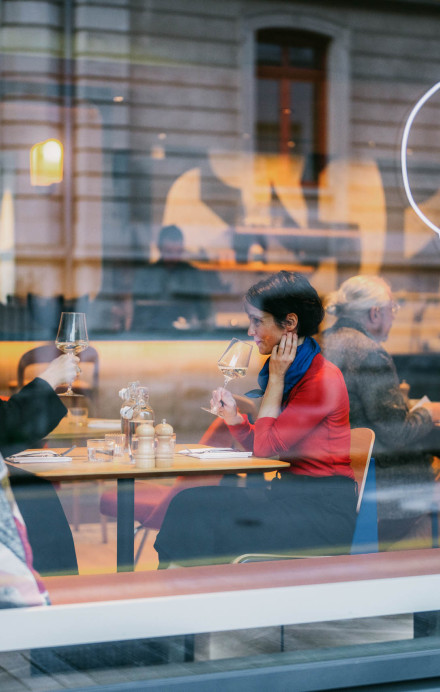 Glasfront eines Restaurants mit Logo, durch das Glas sind die Gäste im Restaurant zu sehen