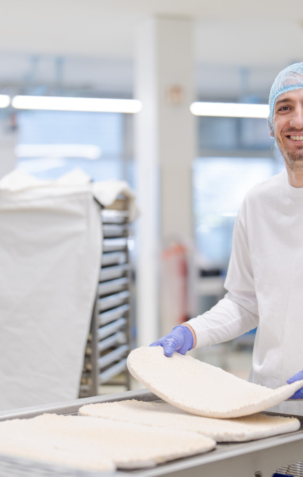Mann mit Produktionskleidung und Kopfhaube steht vor einer Produktionsmaschine