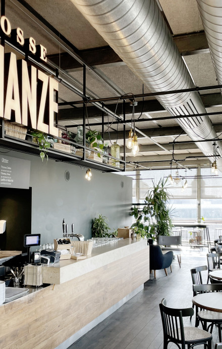 Ansicht Café-Bar mit grossem Logo Grosse Schanze, kleinen runden Tischen und Stühlen