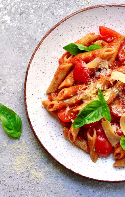 Penne mit Tomatensauce und Basilikum auf grauem Hintergrund