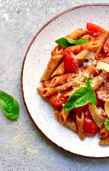 Penne mit Tomatensauce und Basilikum auf grauem Hintergrund