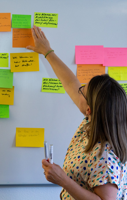 Frau steht an einem Whiteboard und klebt bunte Haftnotizen auf