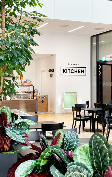 Bild Innenansicht Restaurant Flavour Kitchen in Bern mit Tischen bunten Pflanzen im Vordergrund und Theke im Hintergrund