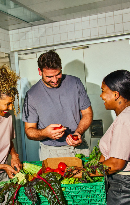 Zwei Frauen und ein Mann stehen in der Küche und rüsten Gemüse.