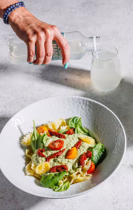 Teller mit Pasta und Hand, die etwas eingiesst