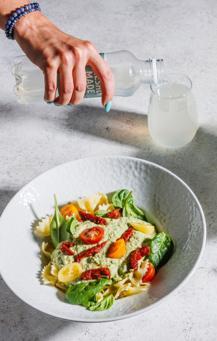 Teller mit Pasta und Hand, die etwas eingiesst