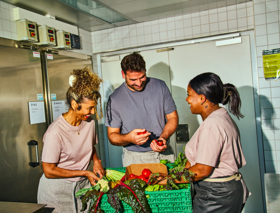 Zwei Frauen und ein Mann stehen in der Küche und rüsten Gemüse.